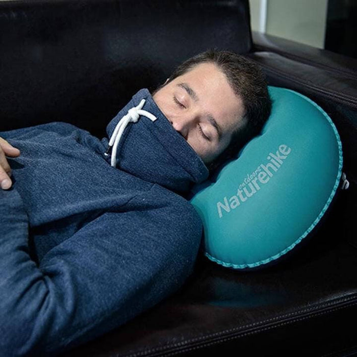 Man napping on a couch using a teal Naturehike inflatable camp pillow