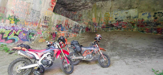 Two loaded dual sport motorcycles parked in the graffiti-covered Marblehead Quarry cave in the Kootenays