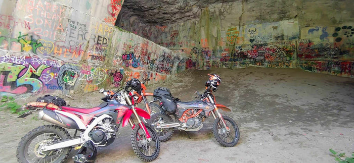 Two loaded dual sport motorcycles parked in the graffiti-covered Marblehead Quarry cave in the Kootenays