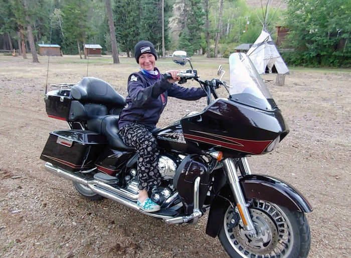 Smiling rider on a Harley-Davidson touring motorcycle at a forested campsite with a tipi behind