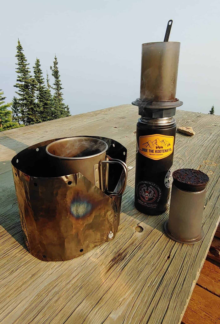Aeropress Go coffee maker brewing on a mountaintop picnic table with an Ride the Kootenays sticker