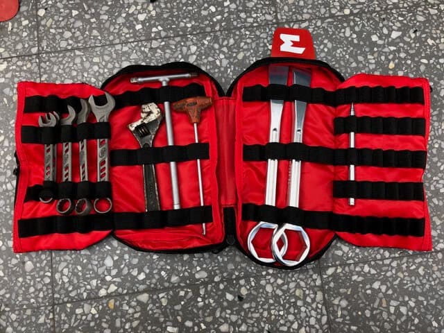 Open red motorcycle tool roll laid out with wrenches, tire levers and a T-handle