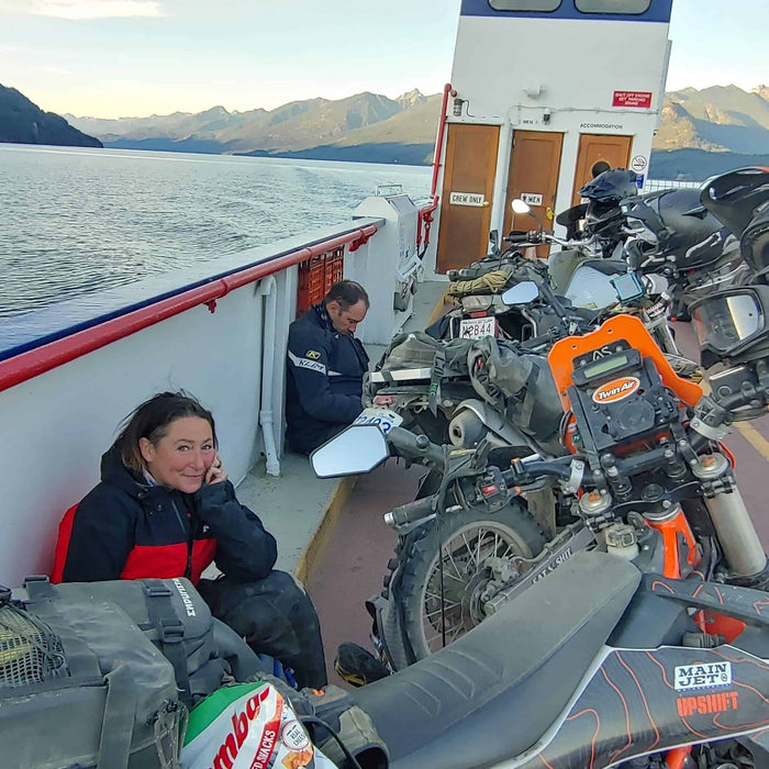 Riders and loaded adventure motorcycles on the deck of the Kootenay Lake ferry at sunrise