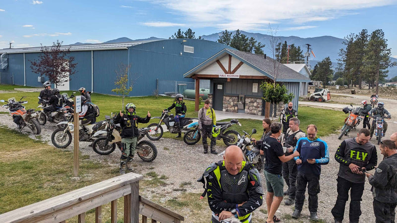 Group of adventure and dual sport riders parked by a public washroom building below mountains at a 2025 dualsport rally