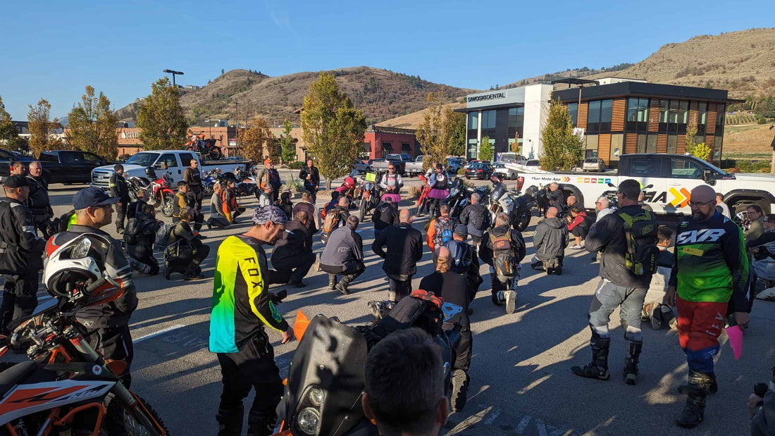 Adventure riders kneeling in a paved parking lot for a rider meeting at a 2024 BC dualsport rally