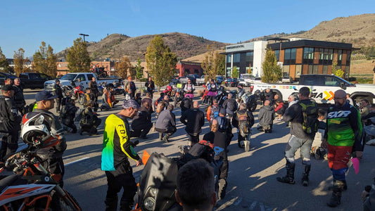 Adventure riders kneeling in a paved parking lot for a rider meeting at a 2024 BC dualsport rally