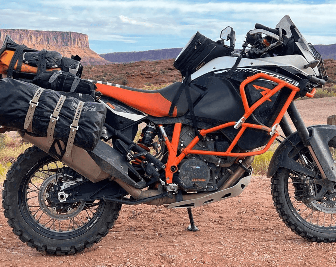 KTM 1190 Adventure motorcycle loaded with Titan Strap secured luggage parked on red desert dirt below mesa cliffs