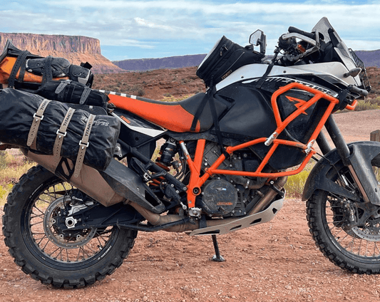 KTM 1190 Adventure motorcycle loaded with Titan Strap secured luggage parked on red desert dirt below mesa cliffs