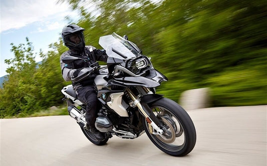 Rider on a black BMW R 1200 GS adventure motorcycle leaning through a corner on a tree lined road