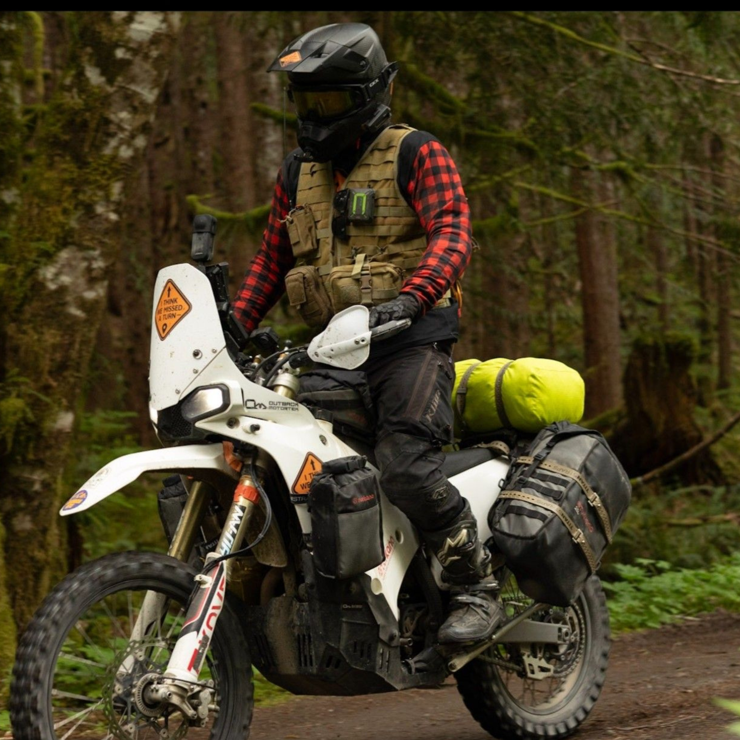 Rider in the ITWMAT Lumbersquatch plaid jersey and tactical vest on a loaded Kove 450 Rally on a forest trail