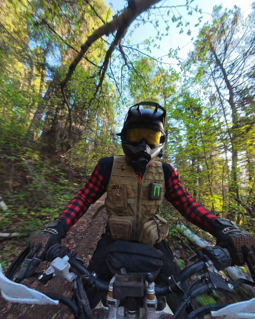 Rider wearing the khaki MOLLE utility vest loaded with pouches, riding a forest trail on the Trans Canada Adventure Trail