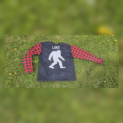 Back of the ITWMAT Lumbersquatch ADV jersey with white Bigfoot graphic and LUKE name and red plaid sleeves on grass