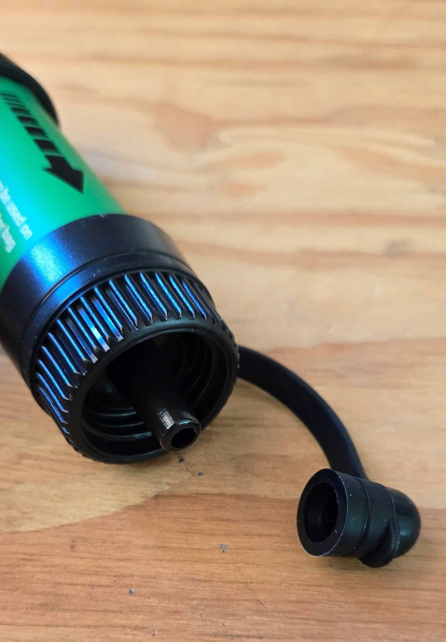 Close-up of the green Ultralight Water Filter Straw outlet end with extension tube and cap on a wood table
